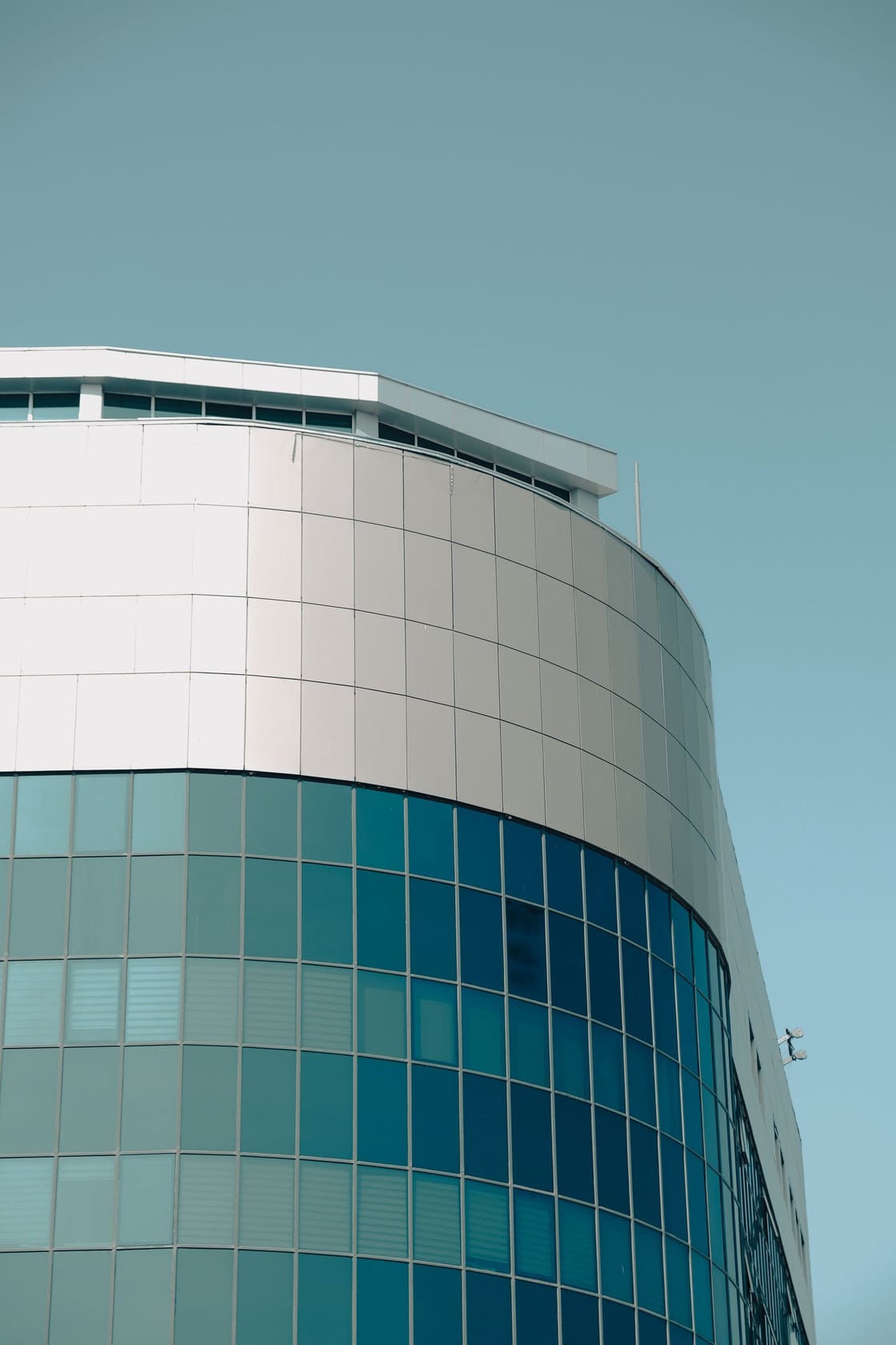 Fachada curva de un edificio contemporáneo con paneles de cristal ante un cielo azul