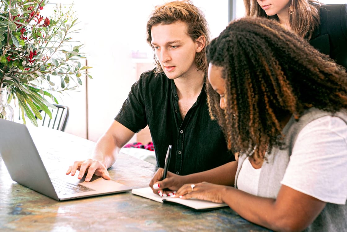 Menschen besprechen gemeinsam eine Idee am Laptop und halten Notizen fest