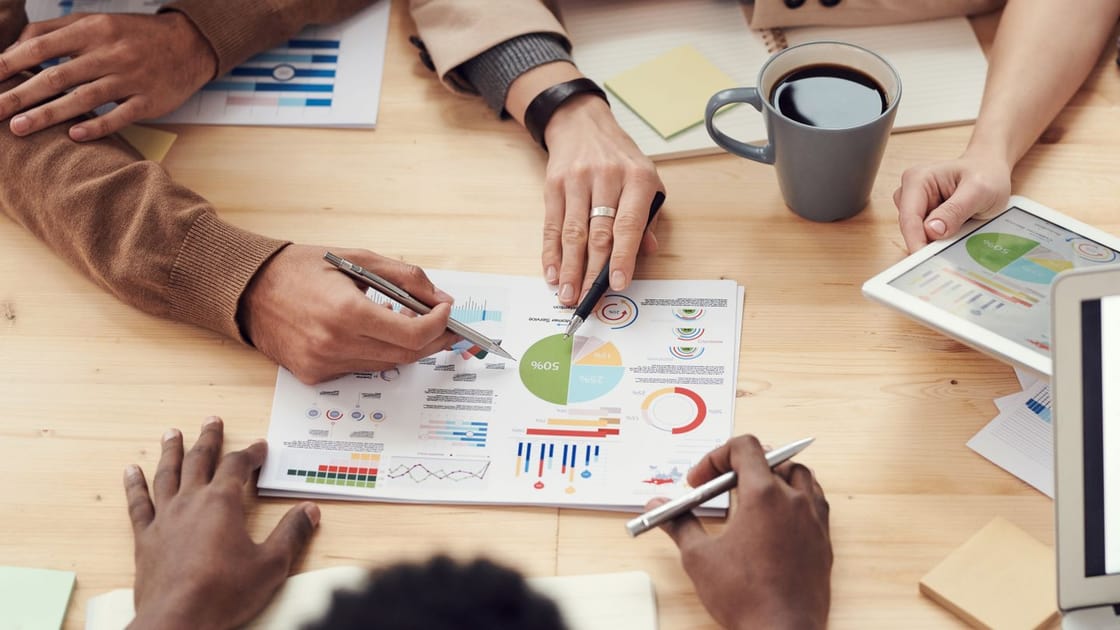 Personas revisan informes, gráficos y planes en una mesa.
