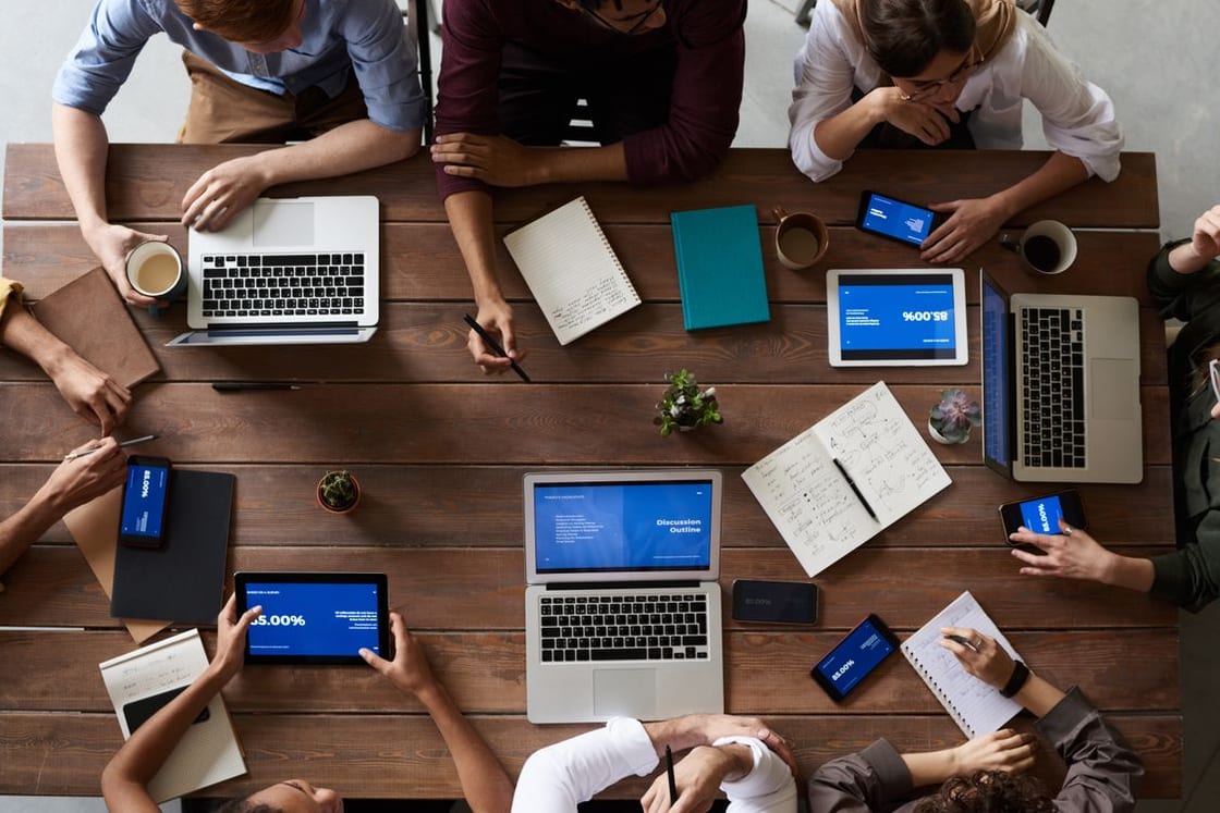 A team plans around a table with laptops, tablets and notebooks.