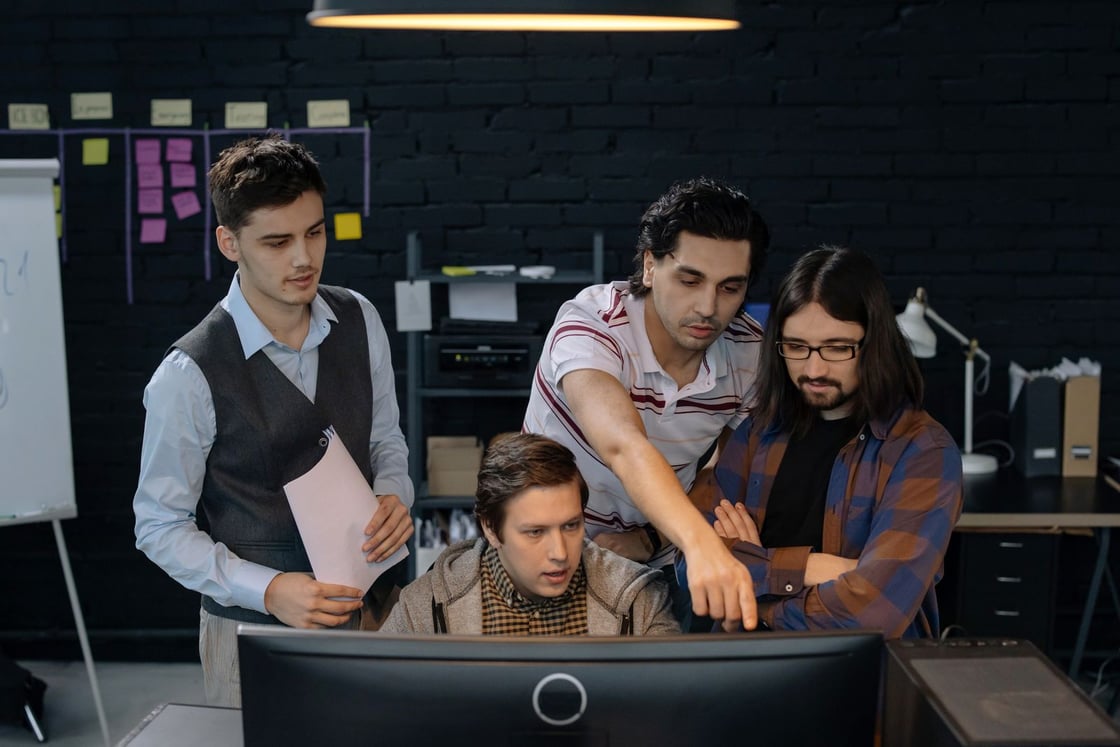 Cuatro personas comentan juntas un proyecto frente a una pantalla